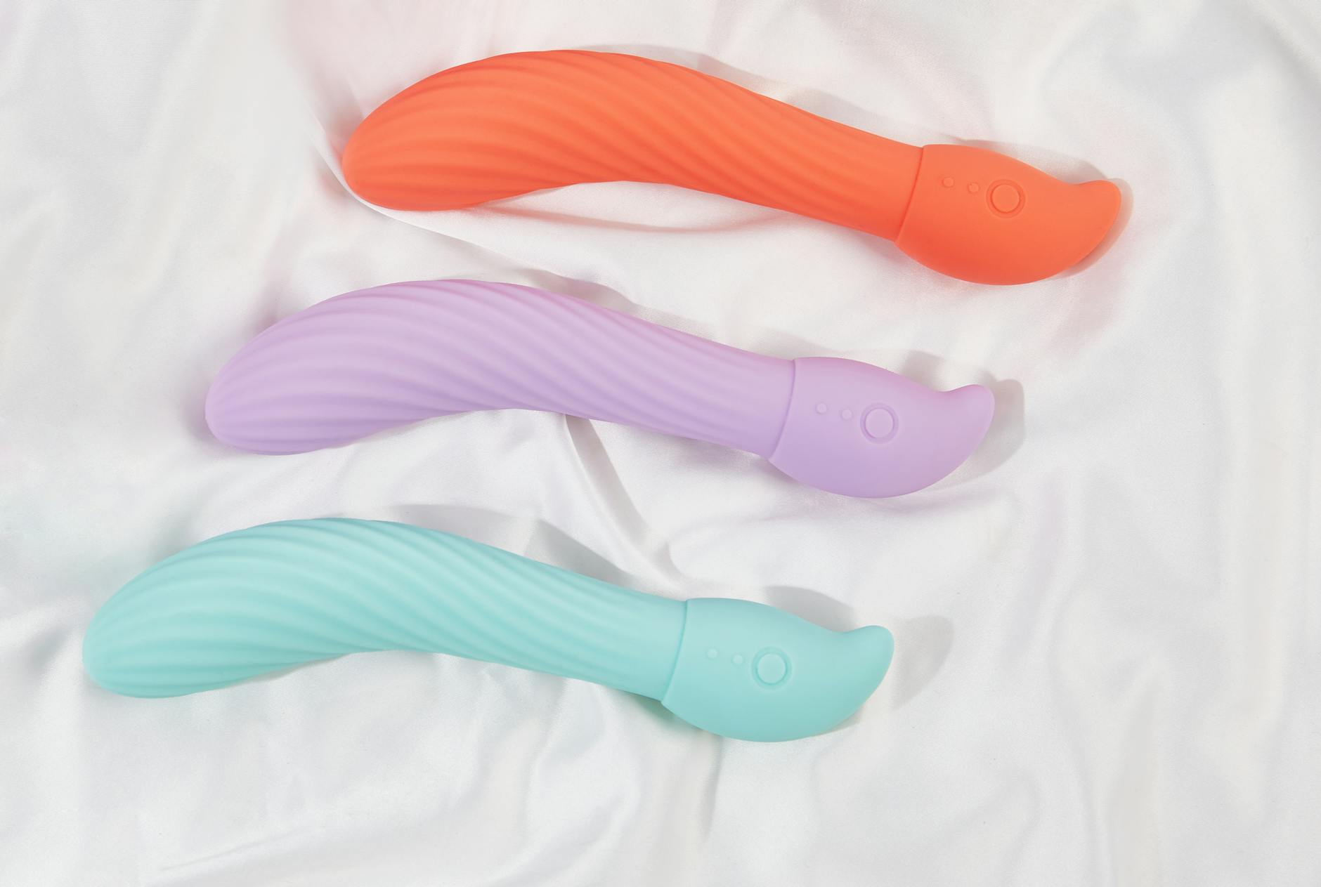 Three colorful vibrators arranged on white fabric, highlighting their smooth texture and design variety.