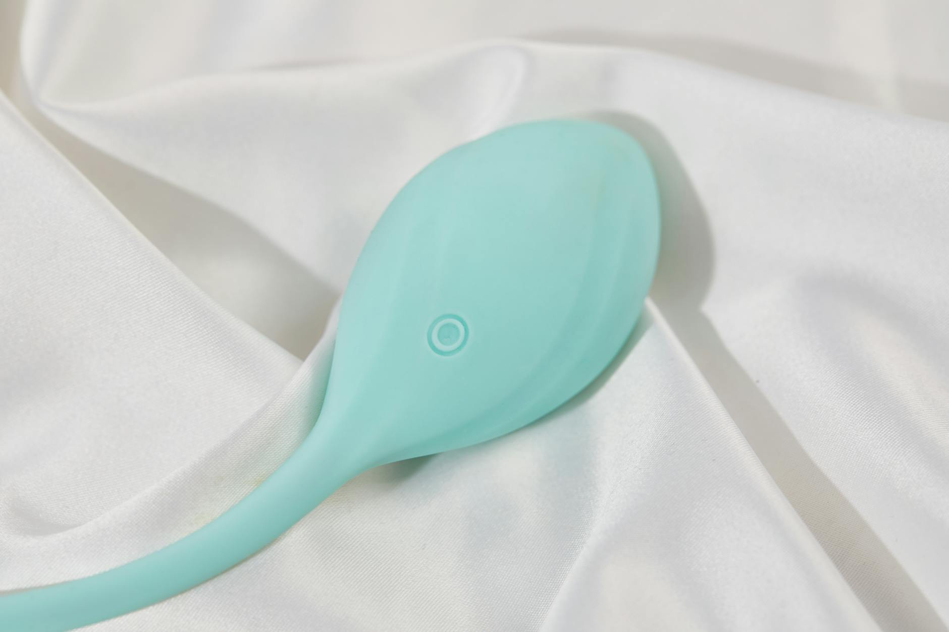 A teal clitoral vibrator on soft white silk fabric, symbolizing intimate self-care