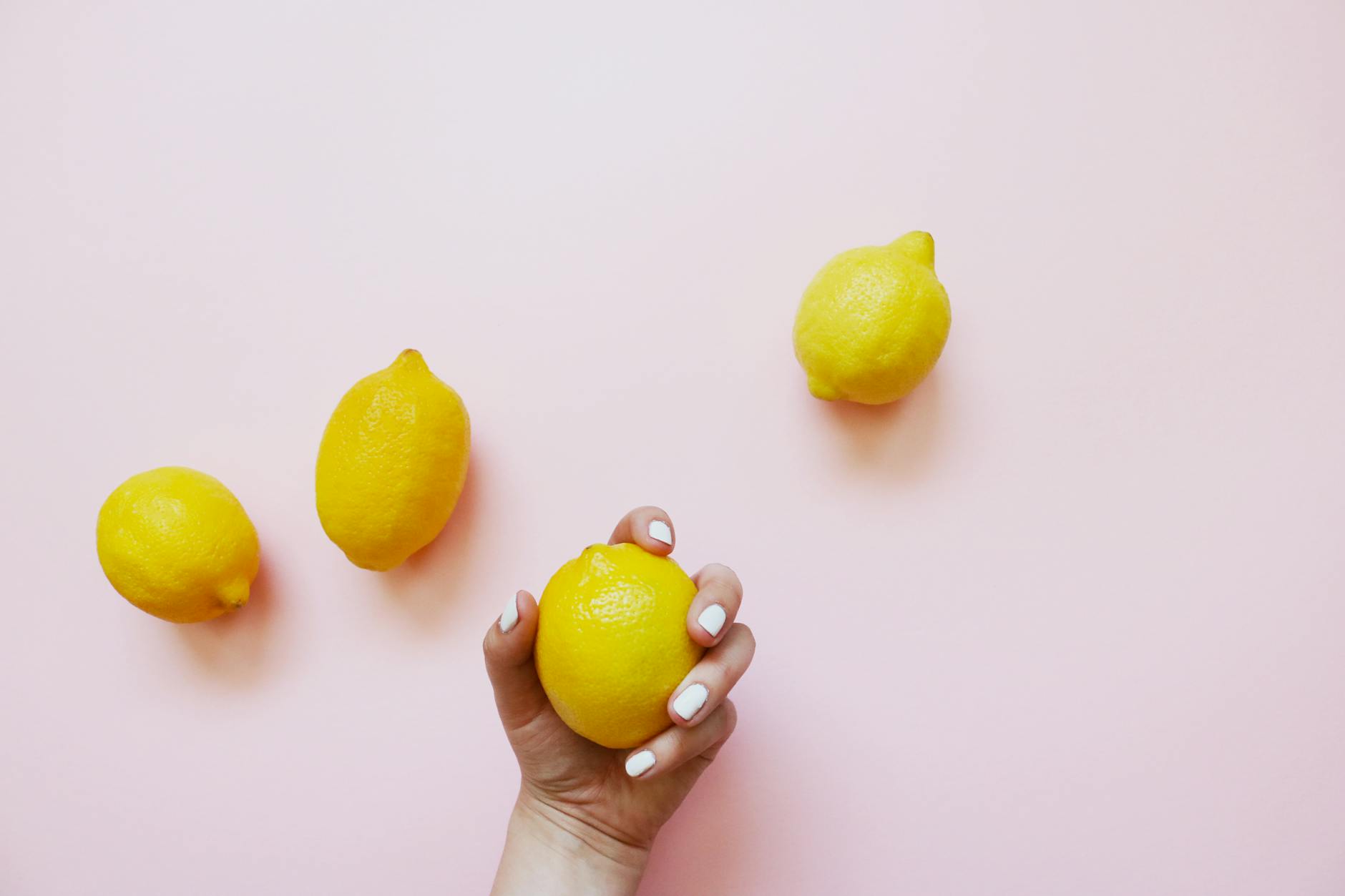 A hand holding a bright lemon on a soft pink background, symbolizing fresh starts and pleasure