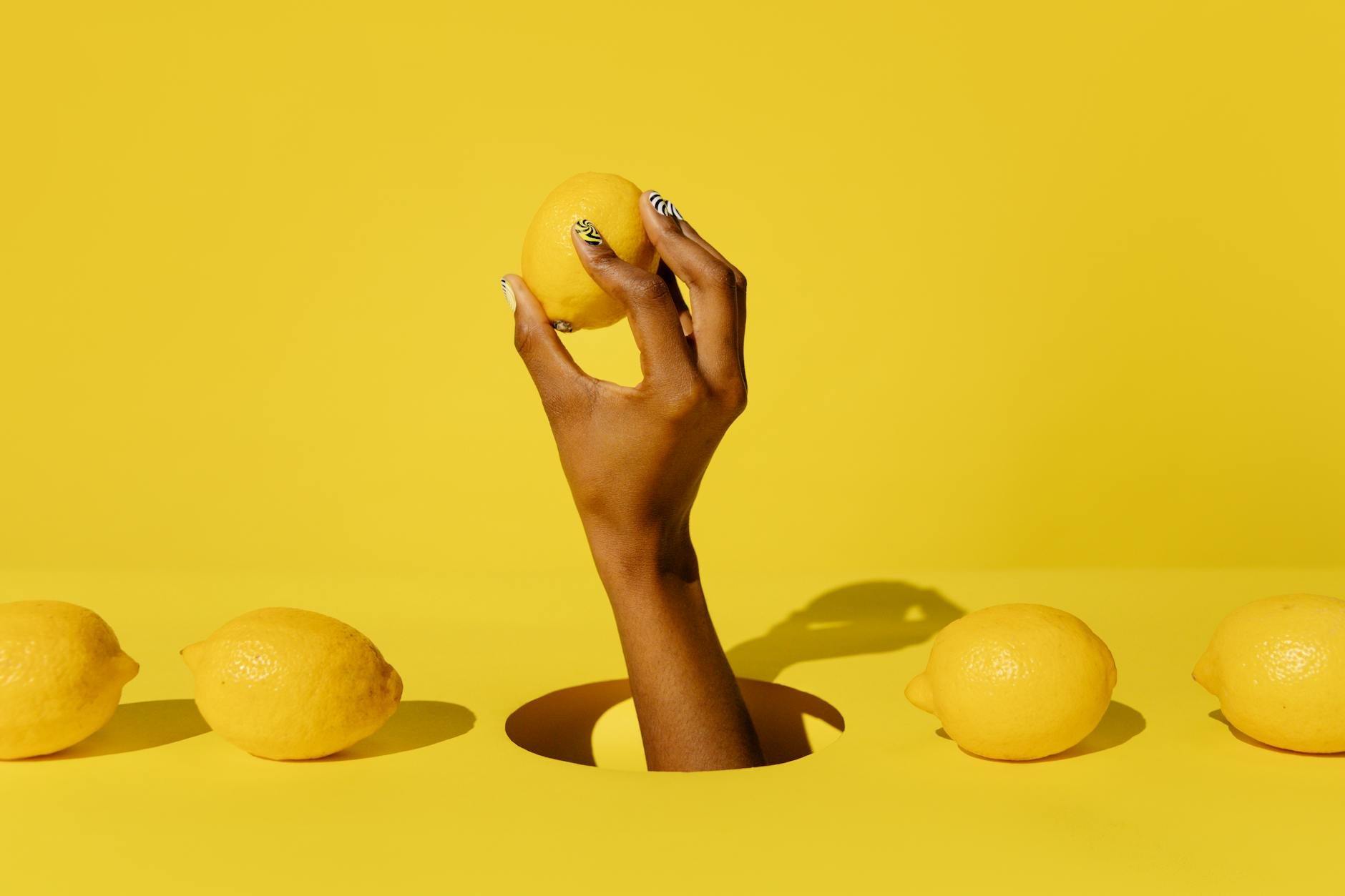 A hand holding a fresh lemon against a vivid yellow background, symbolizing natural sexual vitality and pleasure.