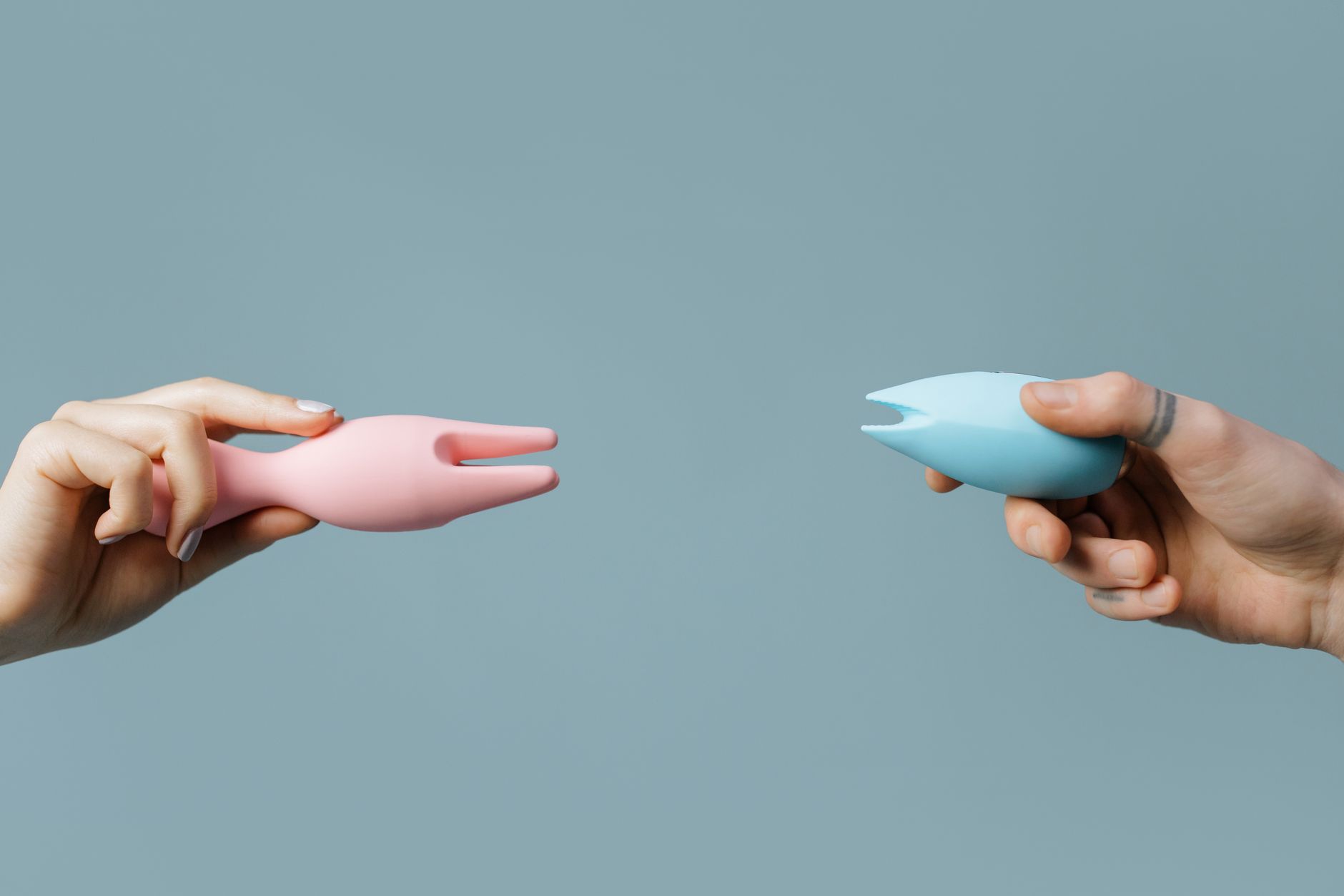 Hands holding colorful vibrators against a pastel background representing personal pleasure choices