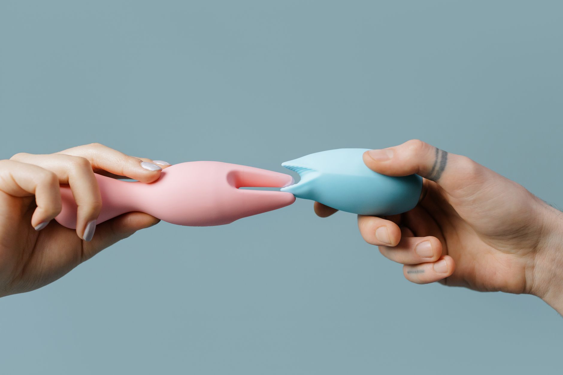 Mão segurando um vibrador de sucção de cor azul contra fundo roxo