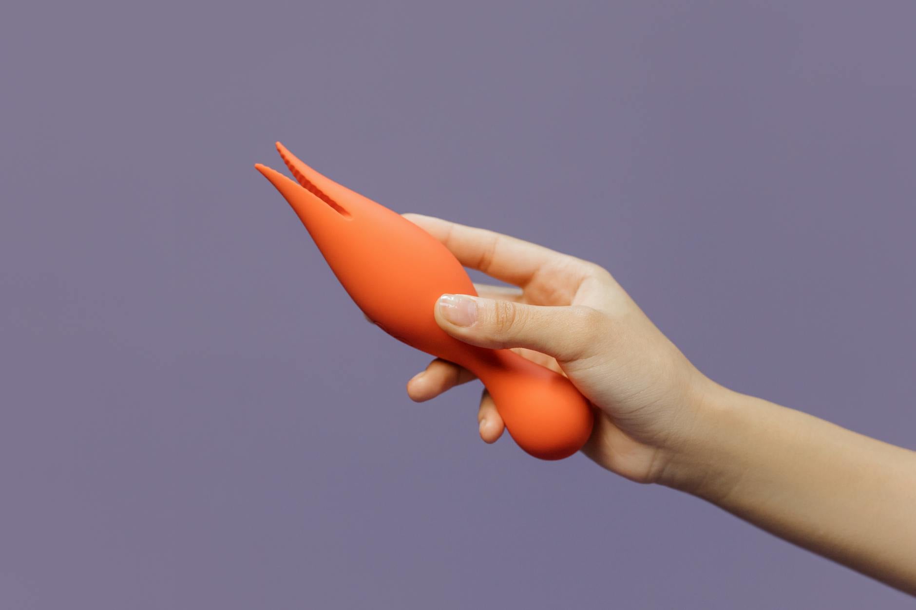 A hand holding a lemon vibrator against a minimalistic purple backdrop