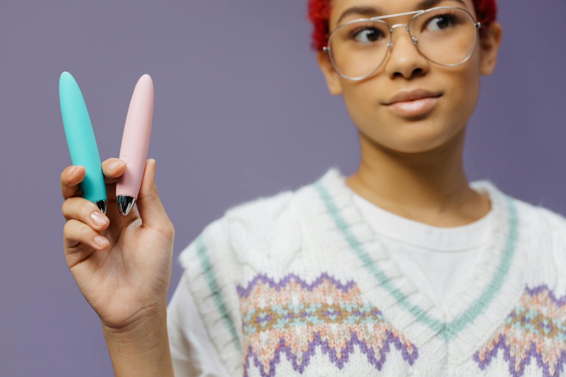 A woman holding colorful vibrators against a purple background, representing diverse sexual wellness tools for travel.