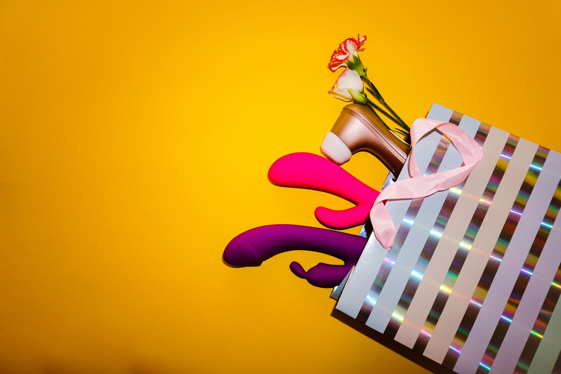 Colorful lemon vibrators with flowers in a holographic gift bag on a bold yellow background