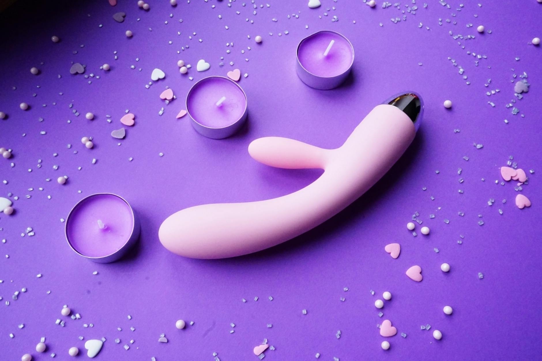 Pink lemon vibrator surrounded by candles and heart confetti on purple background for intimate foreplay moments